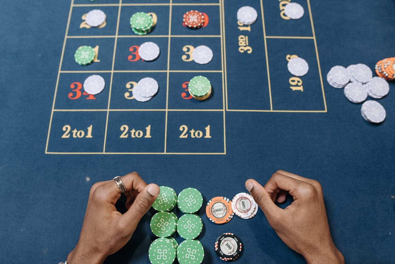 Hands arranging poker chips on a colorful casino gaming table, top view.
